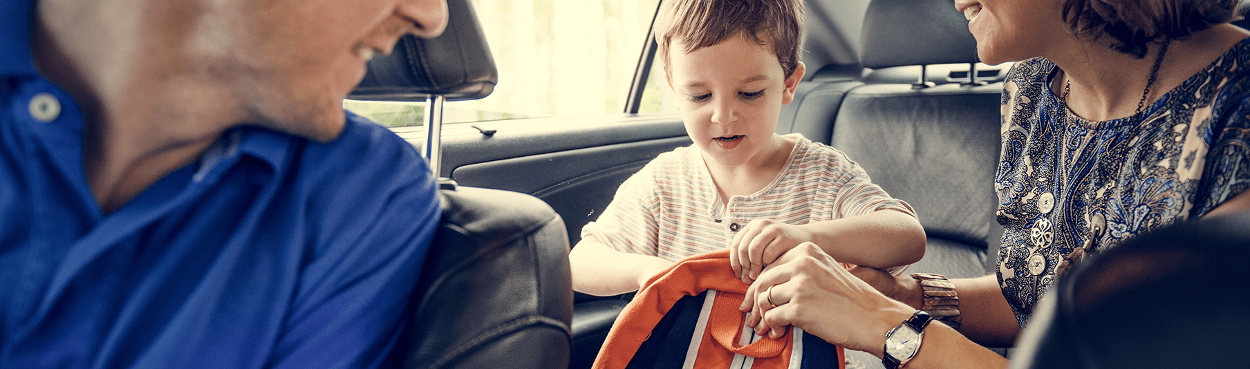 Motor Insurance: A family within their car, the parents helping their son with his backpack