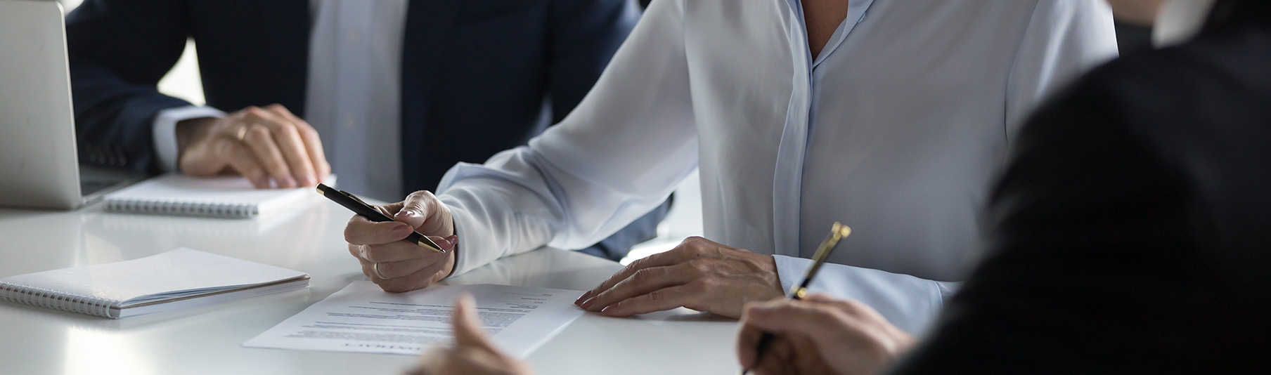 Terms of Business: A business woman sitting with colleagues, about to sign a document 