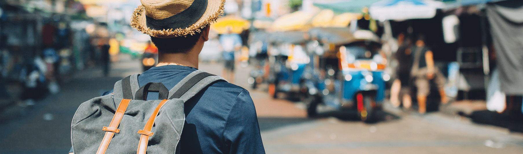 Travel Insurance: A man with a straw hat on his holiday, observing a busy market 